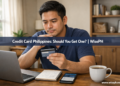 A young Filipino man thoughtfully holding a credit card at his home desk, weighing the decision of whether to get one.