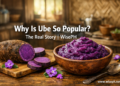 A bowl of freshly made Filipino ube halaya beside a raw ube tuber on a wooden table, showcasing the deep purple color of real Dioscorea alata.